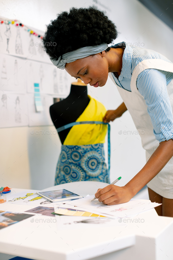 African american female graphic designer writing on paper while measuring mannequin