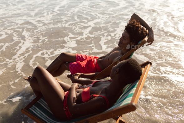 African-american couple interacting with each other while relaxing in a beach chair
