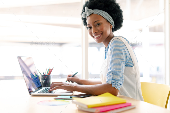 African american female graphic designer using graphic tablet and laptop at desk