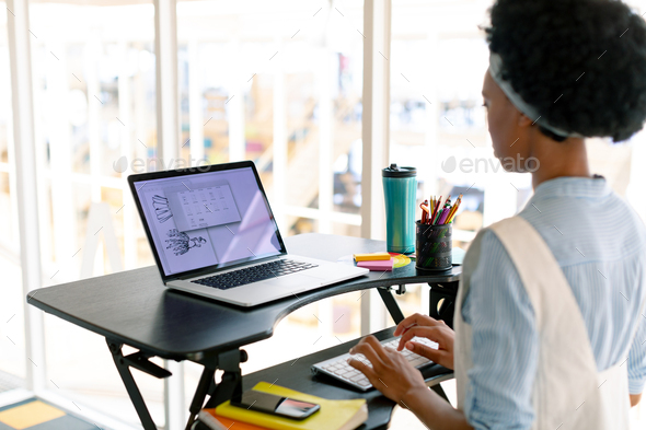 Side view of African american female graphic designer working on laptop at desk in office