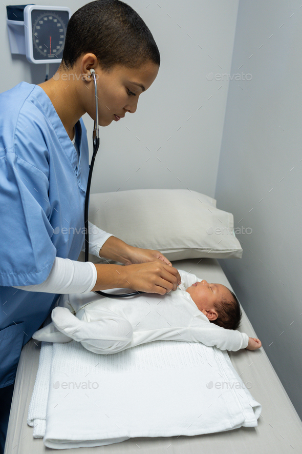 Mixed-race female doctor examining baby with stethoscope in medical examination room