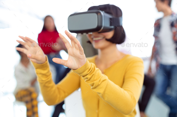 Front view of happy young Asian businesswoman using virtual reality headset in a modern office