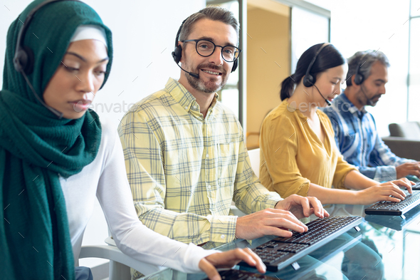 Side view of diverse customer service executives talking on headset at desk in office