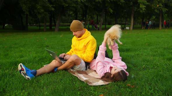 Young Students Sit on the Grass with a Dog on the University Campus and Work at a Computer alt