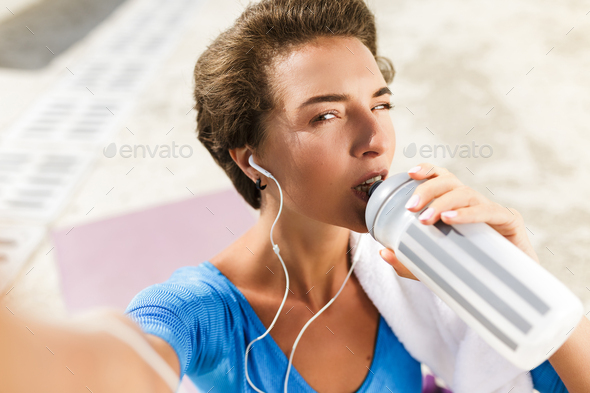Woman in swimsuit sitting on yoga mat drinking water and taking selfie - Stock Photo - Images