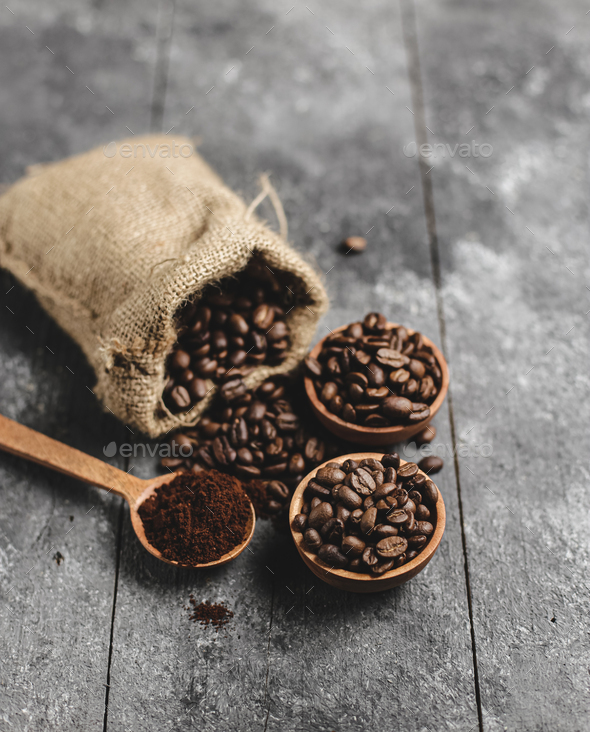 ground coffee beans in wood saucer and wood spoon with grunge black background