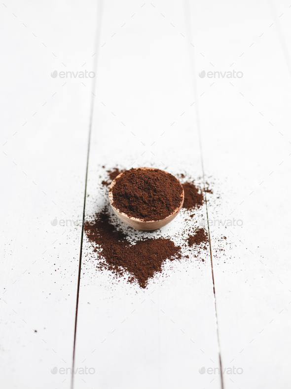 ground coffee in wooden saucer with white wood background