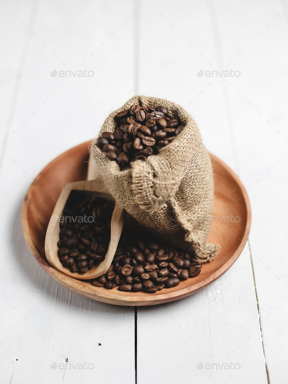 coffee beans in wooden scoop bag and wooden plate with white wood background