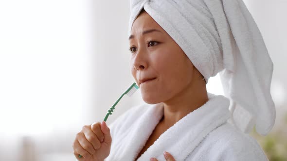 Young Cheerful Asian Woman with Towel on Head Wearing Bathrobe Singing Into Toothbrush Dancing at alt