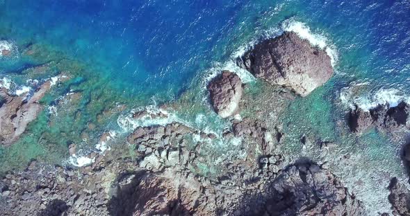 Aerial top view of waves break on rocks in a blue ocean. Sea waves on beautiful beach aerial view alt
