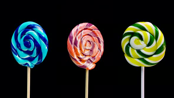 Three Different Lollipops Lollipop Green On A Stick Spinning On A Black Background. alt