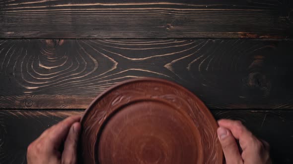 Male Hands Puts and Takes Away Empty Ukrainian Clay Plate From Wooden Table alt
