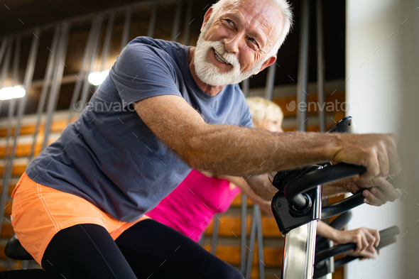 Mature fit people biking in the gym, exercising legs doing cardio workout cycling bikes