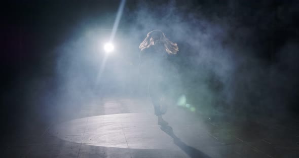 Young female dancer performing wild hip hop dance with light and smoke background alt