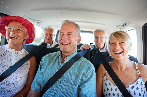 Group Of Senior Friends Sitting In Back Of Van Being Driven To Vacation