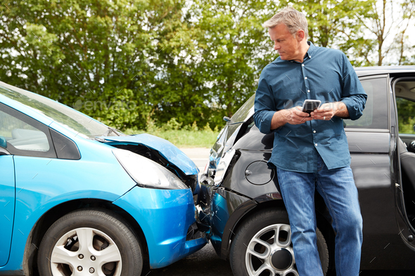 Mature Male Motorist Involved In Car Accident Calling Insurance Company Or Recovery Service