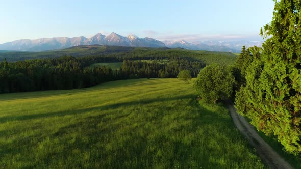 Aerial cinematic view of high mountains and green meadow during sunrise in summer.