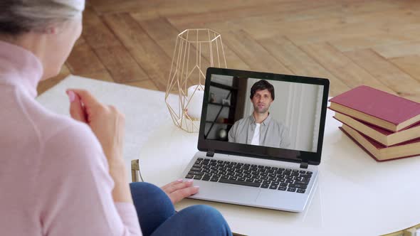 Over the Shoulder View of an Elderly Woman Video Call To a Young Son Using a Laptop. The Concept of alt