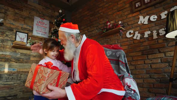 Little Girl Comes To Santa Claus, Presents New Year Gift and Hugs Christmas Grandfather