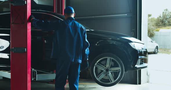 Car Service Worker Lifting Vehicle on Hoist Before Maintenance at Service Workshop alt