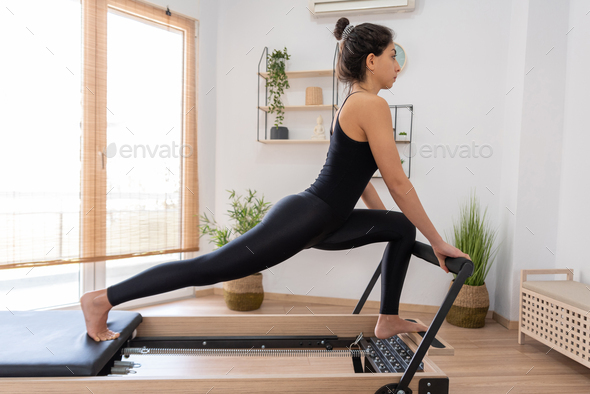Young woman exercising on pilates reformer bed Stock Photo by sianstock