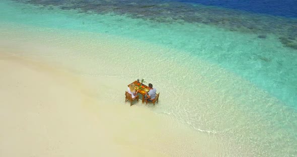 Aerial drone view of a man and woman eating breakfast on a tropical island beach alt