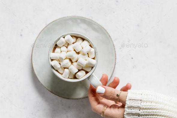 Girl's hand holds a cup of hot chocolate with marshmallow over textured white background - Stock Photo - Images