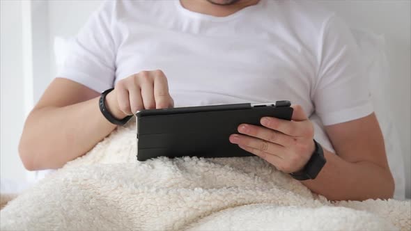 Man Is Relaxing with Tablet in Bed. alt