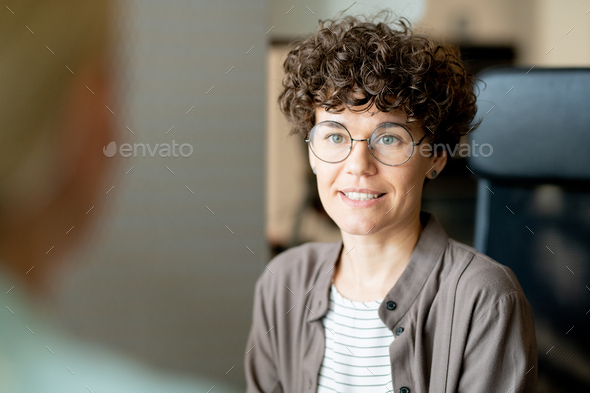 Young confident businesswoman looking at client or partner during interaction