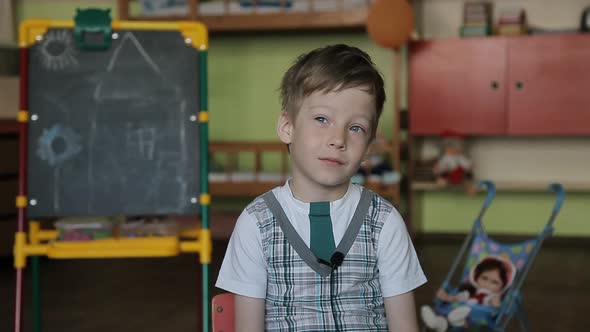 A 6 Year Old Boy Sits on a Chair with a Lapel Microphone on His Clothes and Answers Questions.