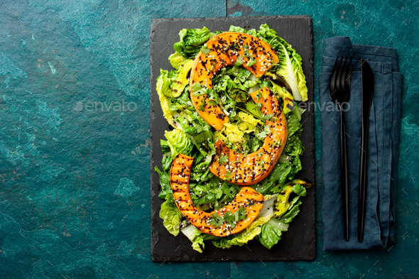 Grilled pumpkin salad with lettuce on black board plate, blue slate background. Autumn menu.