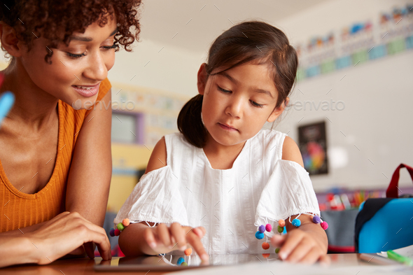 Elementary School Teacher And Female Pupil Drawing Using Digital Tablet In Classroom - Stock Photo - Images