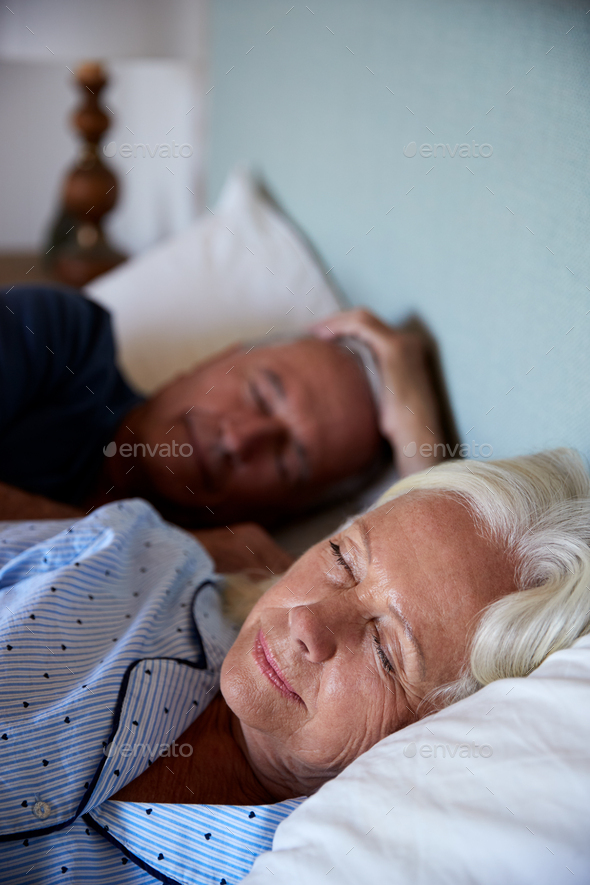 Senior white couple asleep in their bed, waist up, close up, vertical