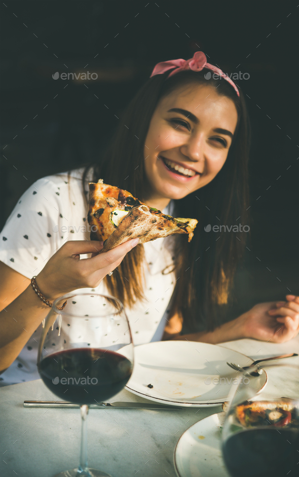 Young happy caucasian woman eating pizza and drinking wine - Stock Photo - Images