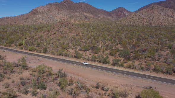 Aerial Side View of Small White Car Moving Along Desert Road
