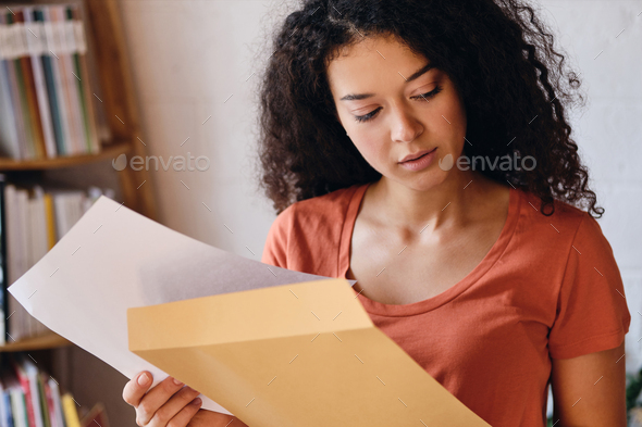 Young pensive lady with in T-shirt thoughtfully looking aside holding letter with exam results