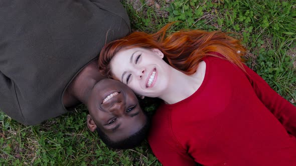 Happy interracial lovers lying on meadow,smiling,laughing-top view alt