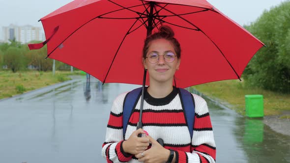 Young Lady Stands Under Red Umbrella on Roadside alt