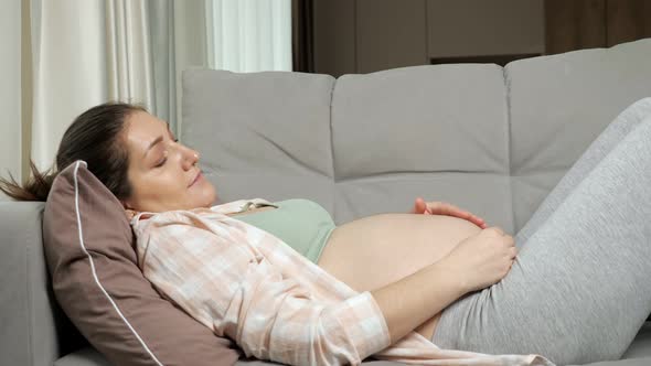 Pregnant Woman Lies on Sofa Stroking Bare Belly Carefully alt
