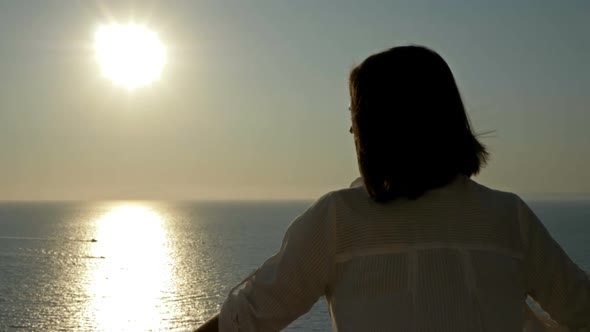 Young Woman Stands on a Balcony with a Beautiful View of the Sea and Mountains alt