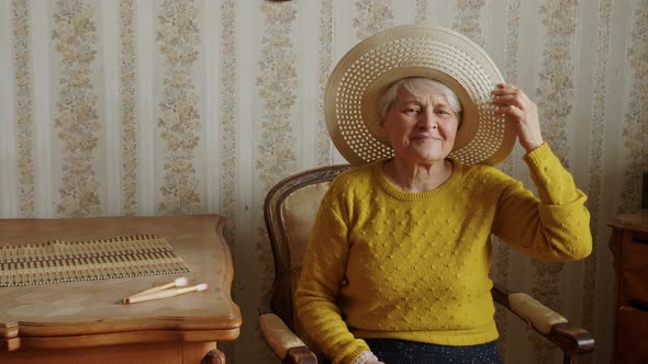 Cute Elder Woman Sitting on the Chair and Adjusting Her Summer Hat Medium Shot Living Room Seniority alt