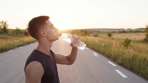 Young Sportsman Drinking Water From a Bottle and Looking Thoughtfully alt