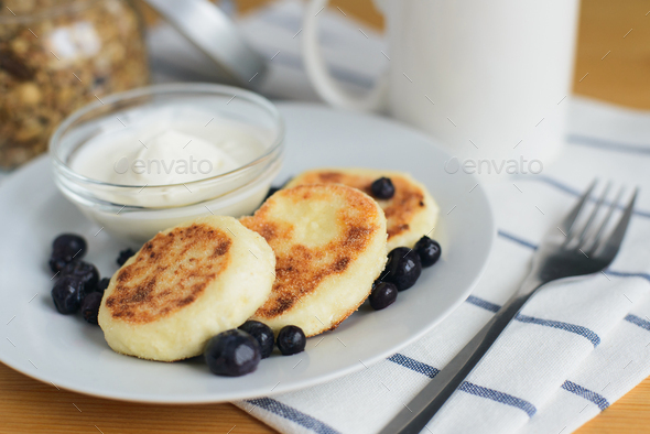 fried circular syrniki, tvorozhniki or cheese cake with sour cream and hot drink - Stock Photo - Images