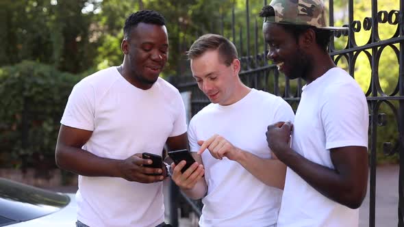 Three Multiracial Students Communicate with Each Other, Look at the Phone and Laugh