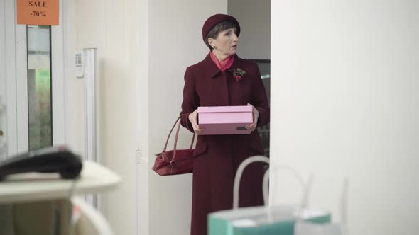 Senior Beautiful Woman Stealing Box From Store. Portrait of Nervous Caucasian Female Client Looking alt