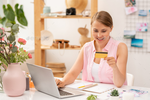 Happy young female online shopper with plastic card entering its number