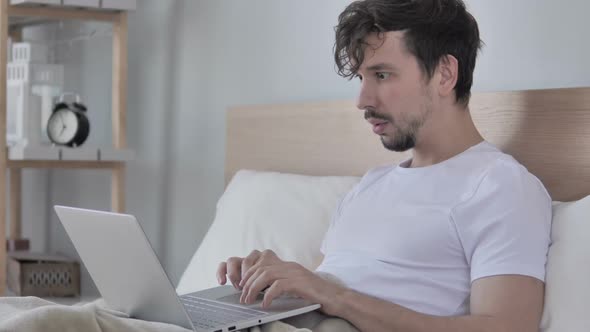 Man Wondering in Shock While Using Laptop in Bed alt
