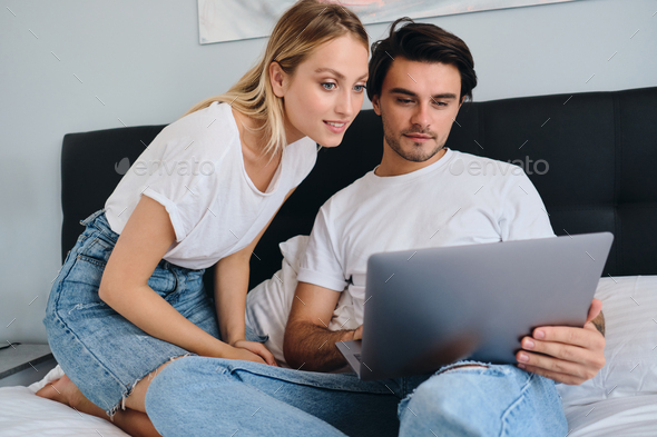 Pretty blond woman amazedly looking in laptop while attractive brunette man working on it