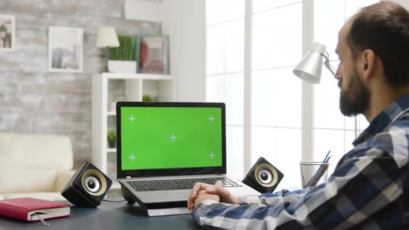 Over the Shoulder Zoom in Shot of Man Looking at Laptop with Green Screen alt