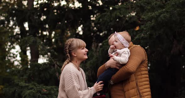 Loving Mother Kissing Her Daughter on Father's Hands in Park.